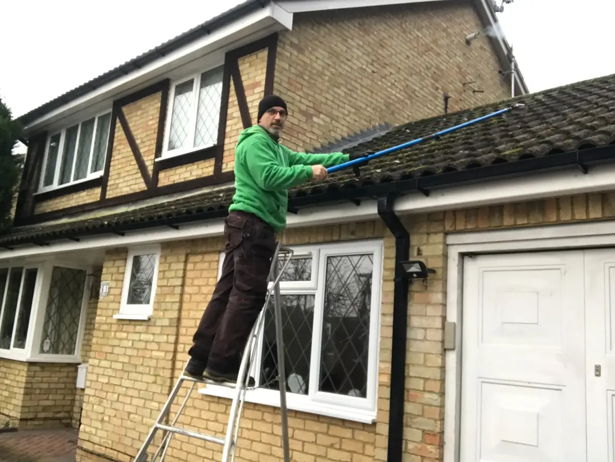 Team removing moss from a tiled roof with poles from ladders